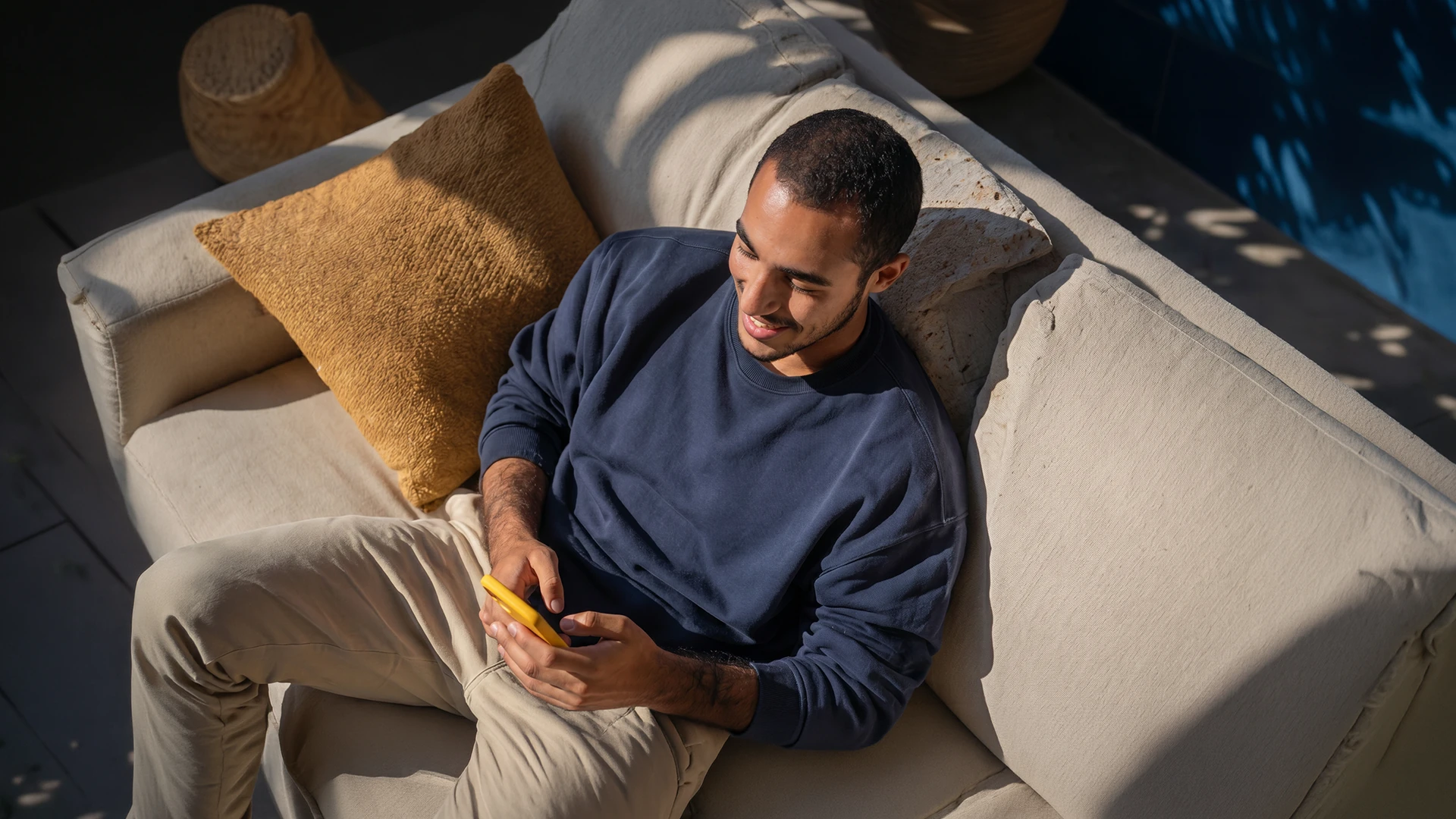 Homem sentado no sofá de casa usando o celular, representando o download do app RecargaPay para fazer Pix parcelado