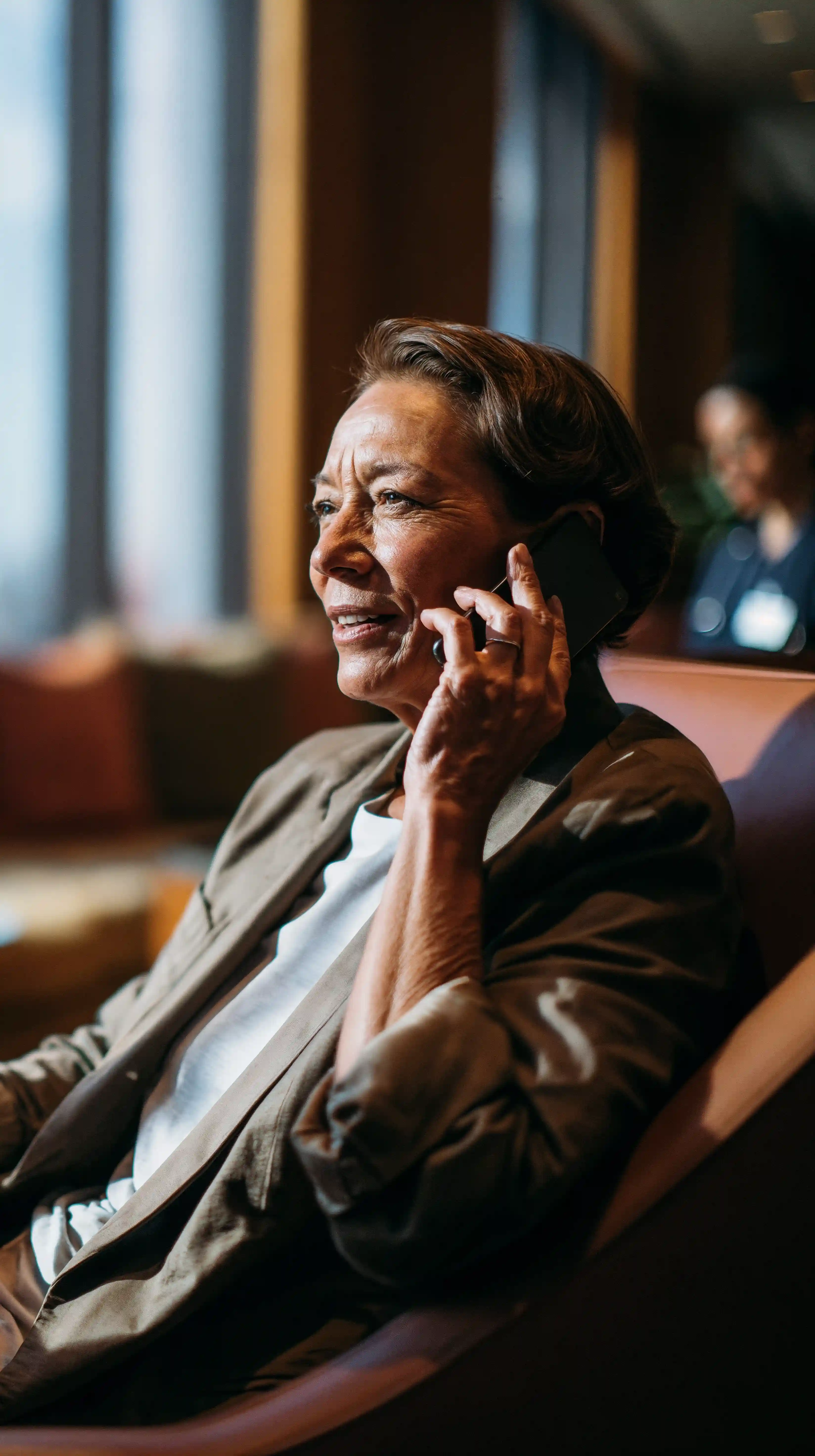 Mulher sorridente falando ao telefone sentada em uma sala de espera de aeroporto