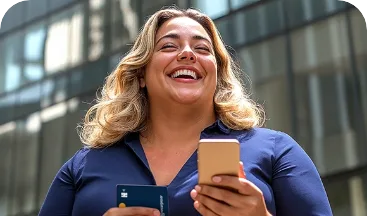 Mulher loira sorrindo, segurando um celular e um cartão de crédito RecargaPay, em frente a prédios