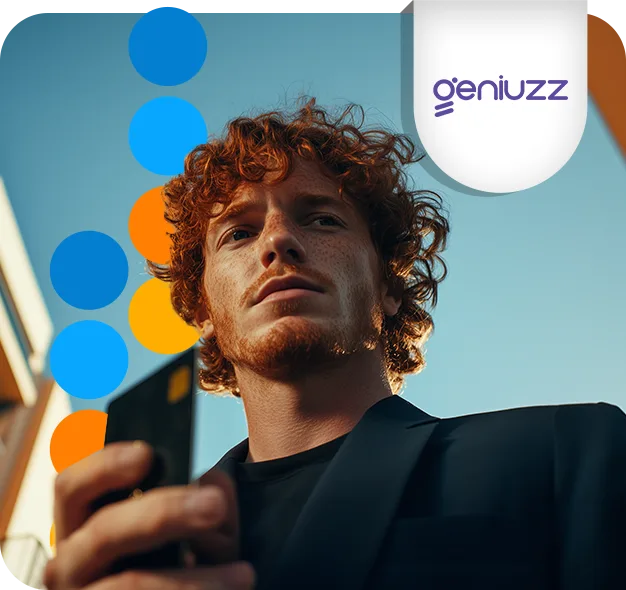 Homem de cabelo ruivo e blazer preto olhando para o celular, contra um céu azul e círculos coloridos