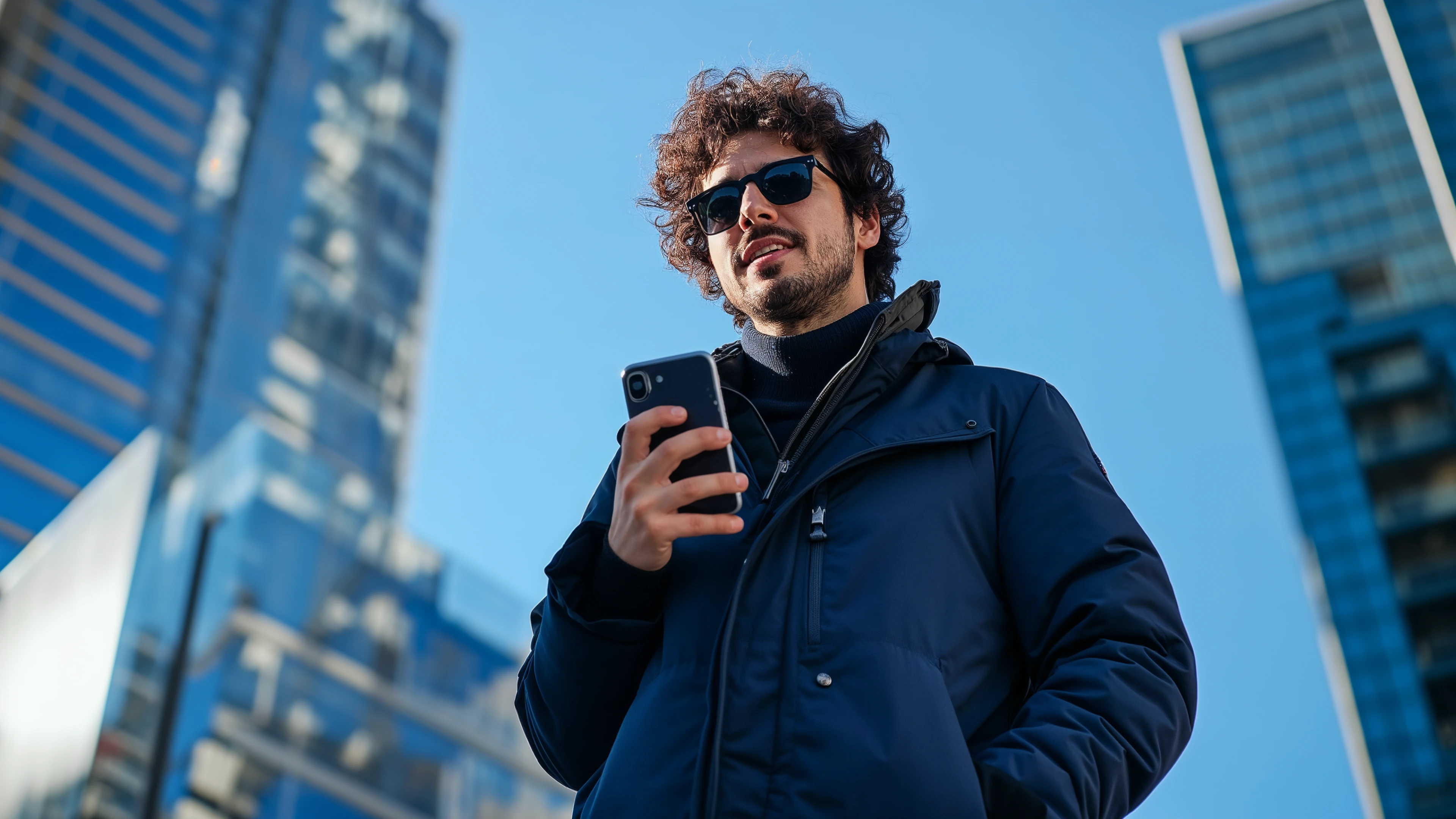 Homem de óculos escuros segurando o celular entre prédios, representando o empréstimo pessoal 100% digital