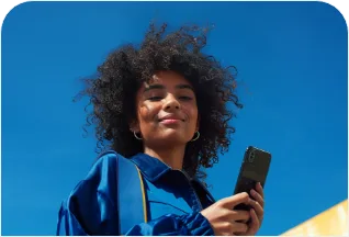 Mulher de cabelo cacheado e jaqueta azul segurando um celular, contra um céu azul