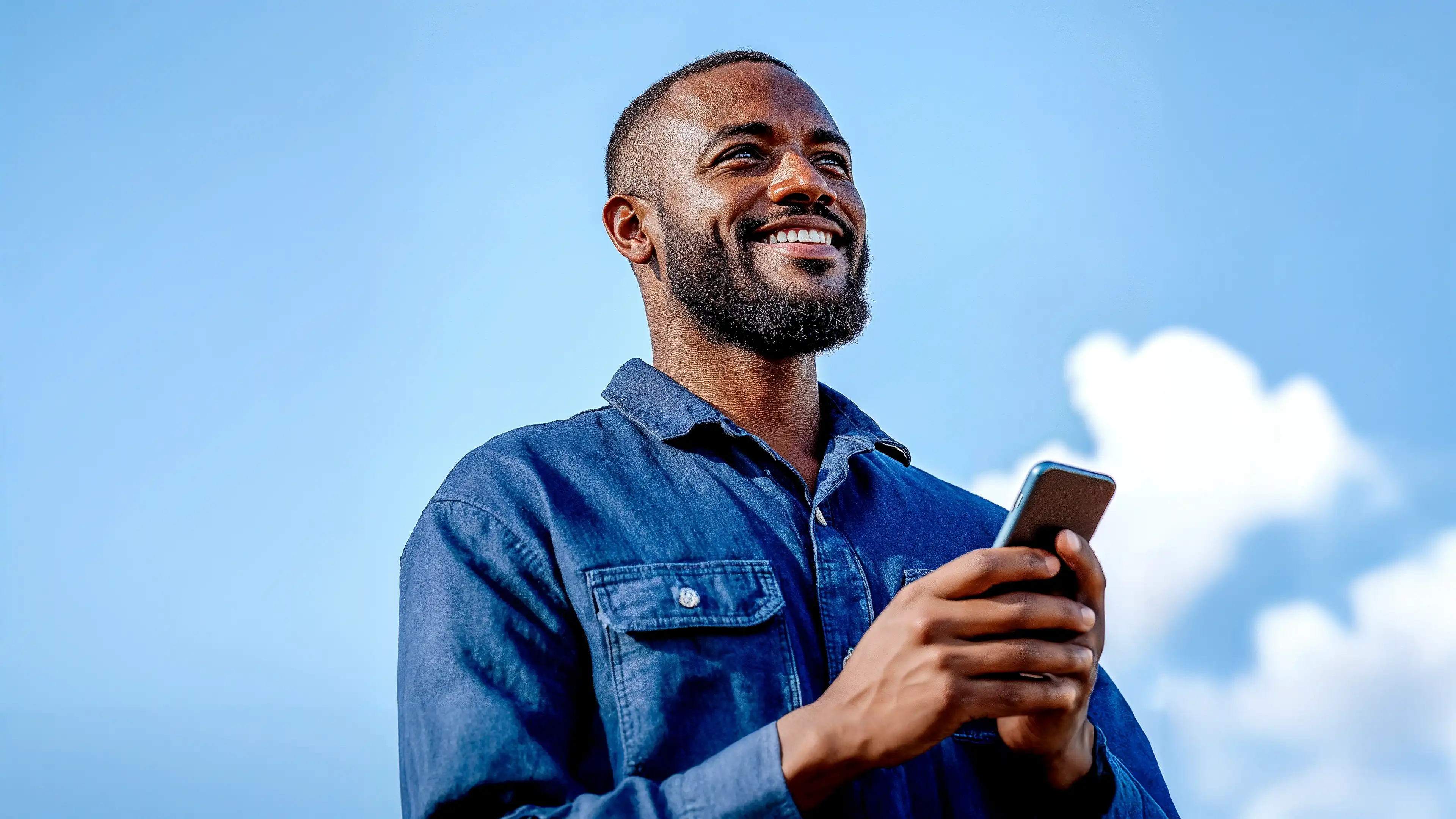 Homem sorrindo enquanto usa o celular ao ar livre.