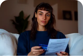 Mulher sentada no sofá segurando uma conta impressa e um cartão de crédito