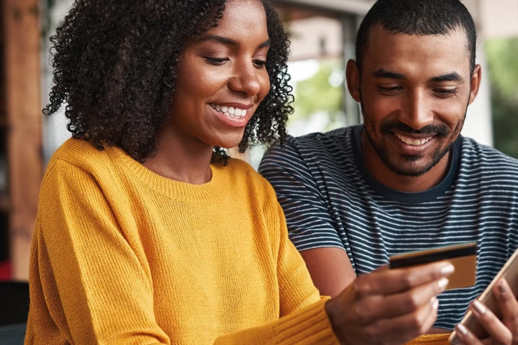 Casal sorrindo enquanto olha um cartão de crédito e o celular, representando o Pix parcelado no cartão