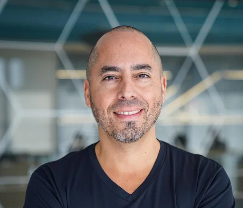 Rodrigo Teijeiro, fundador e CEO do RecargaPay, sorrindo, de camiseta preta, em um escritório com paredes de vidro