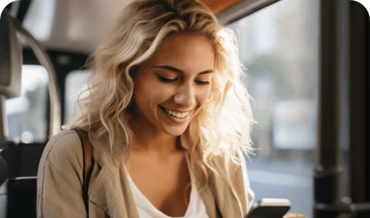 Mulher loira sorrindo enquanto olha para o celular dentro de um ônibus