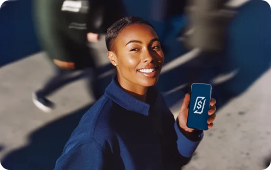 Mulher sorrindo segurando um celular com o app RecargaPay aberto, em uma calçada movimentada