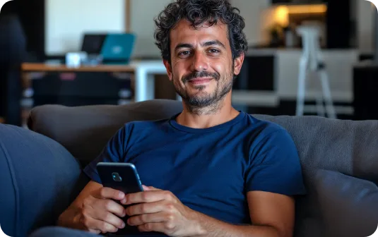 Pessoa sorrindo em casa enquanto usa o celular.