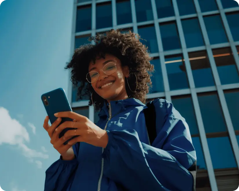 Mulher sorrindo olhando para o celular, demonstrando tranquilidade financeira.